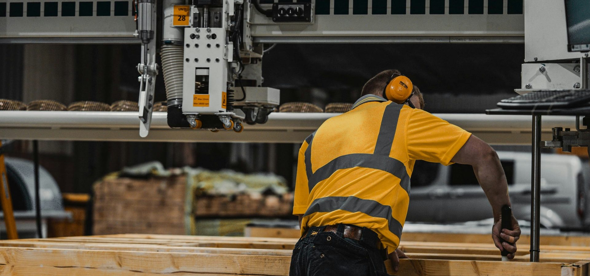 Un ouvrier en gilet haute visibilité travaille sur une machine à bois dans un atelier